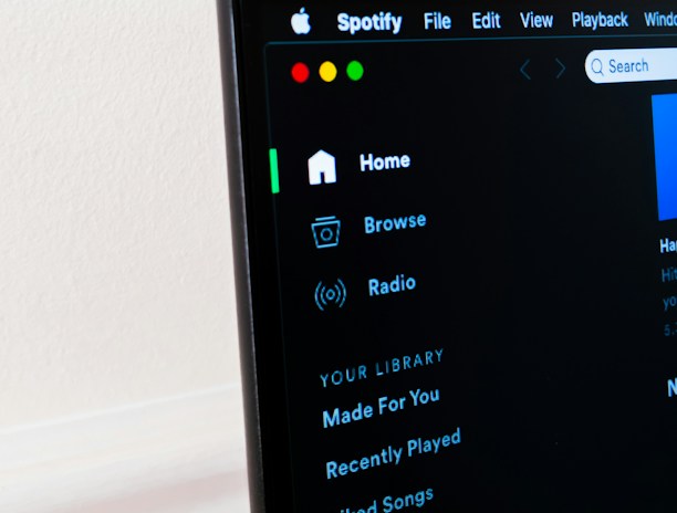A computer screen displays the Spotify application, showing menu options such as Home, Browse, Radio, and Your Library, which includes Made For You, Recently Played, and Liked Songs. The application interface is sleek, with a dark background and white text, alongside green, yellow, and red window control buttons at the top left.